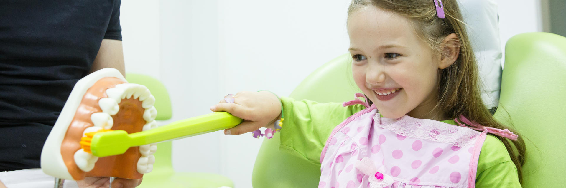 Happy little girl with a dental model and a big toy toothbrush learning how to brush teeth properly.